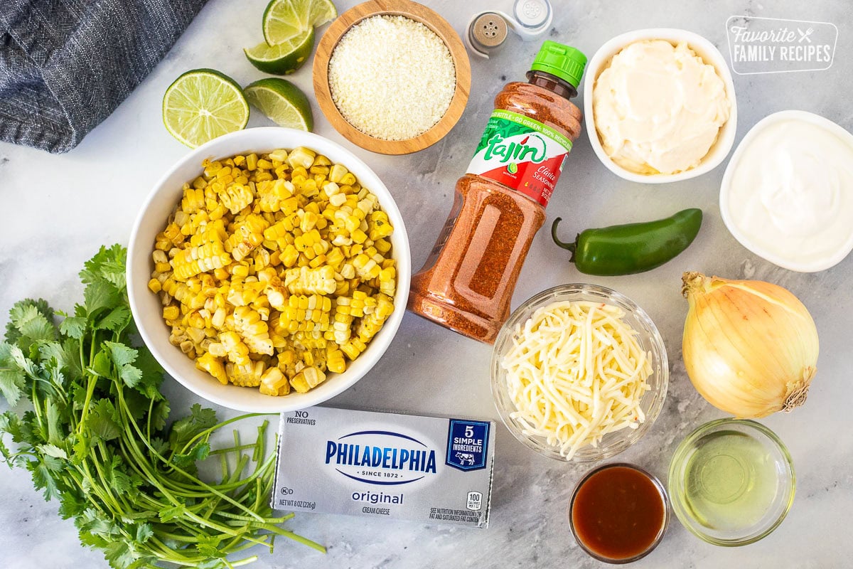 Ingredients to make Mexican Street Corn Dip including sour cream, mayonnaise, jalapeño, onion, oil, pepper jack cheese, Tajin seasoning, cojita cheese, cilantro, cream cheese, hot sauce, salt, pepper and lime.