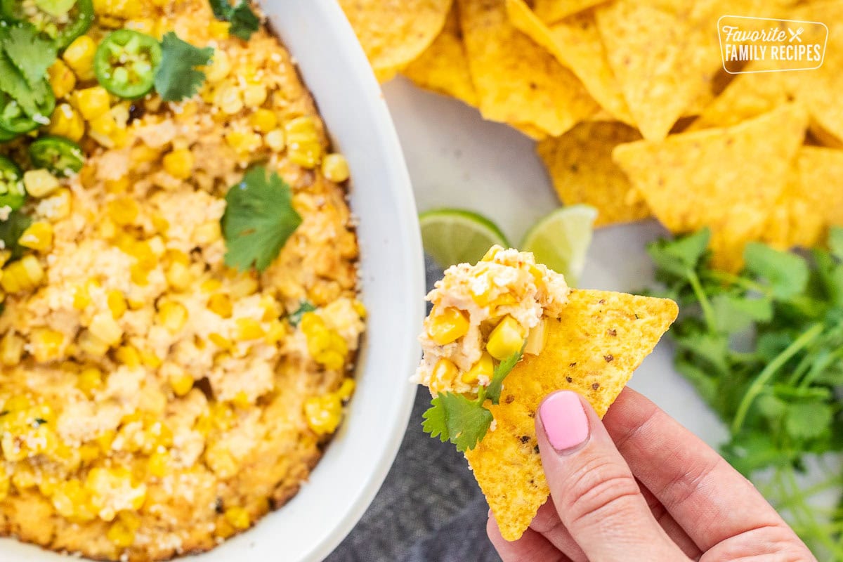 Hand holding a chip with Mexican Street Corn Dip in a dish.