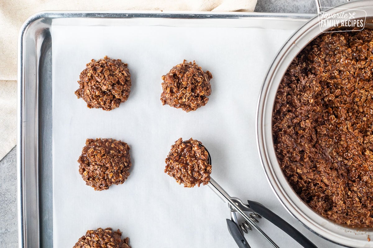 Baking sheet lined with parchment paper with cookie scoop a full of no bake cookies