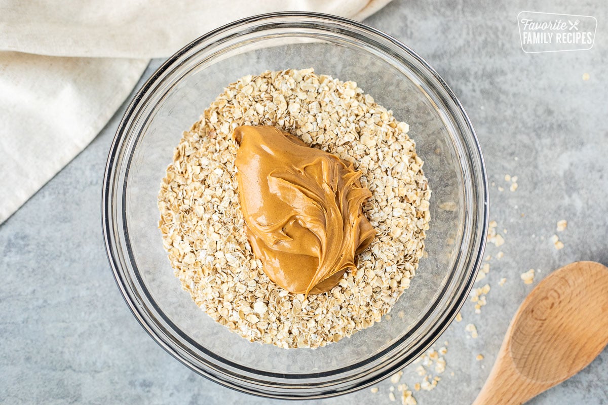 Glass mixing bowl of oatmeal and creamy peanut butter. Wooden spoon on the side.