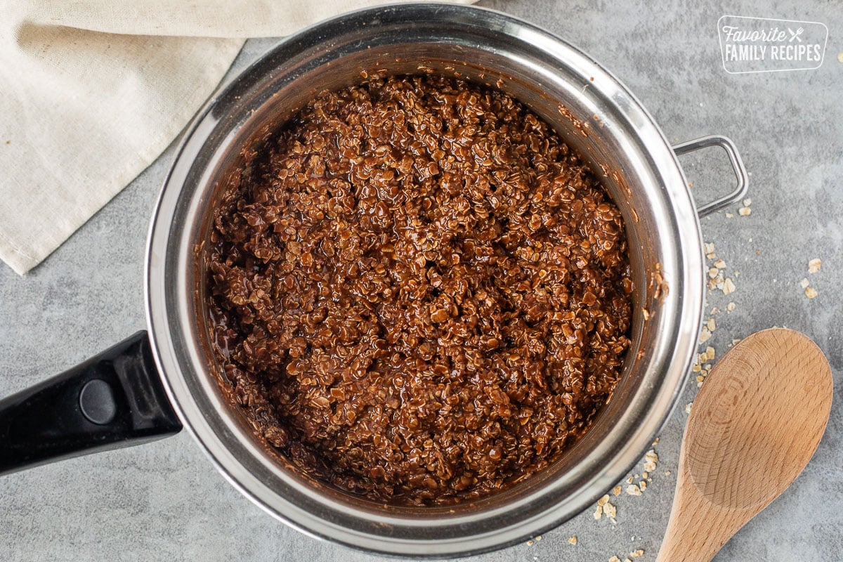 Saucepan with oats, peanut butter and chocolate combined. Wooden spoon on the side.