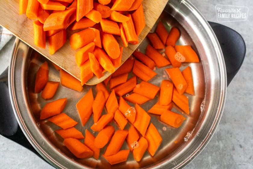 Pouring cut carrots into pan of water.