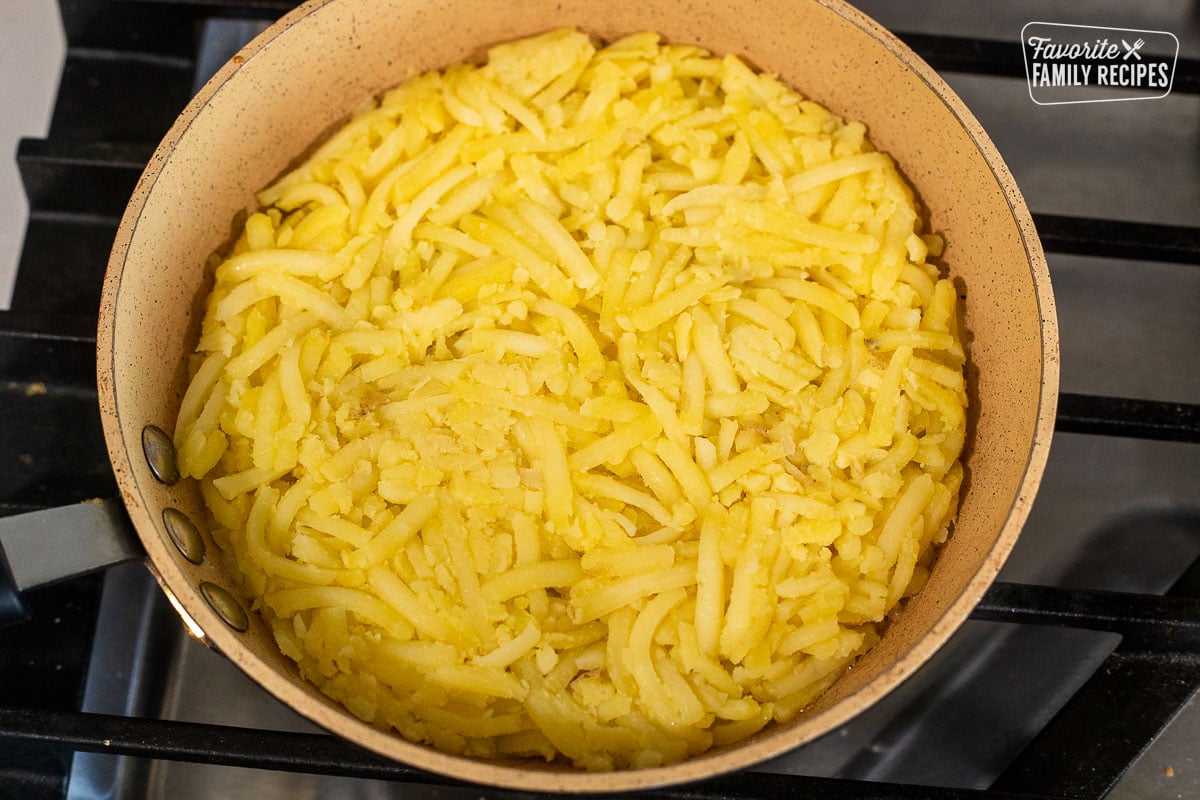 Skillet with shredded potatoes pressed in a circle shape.