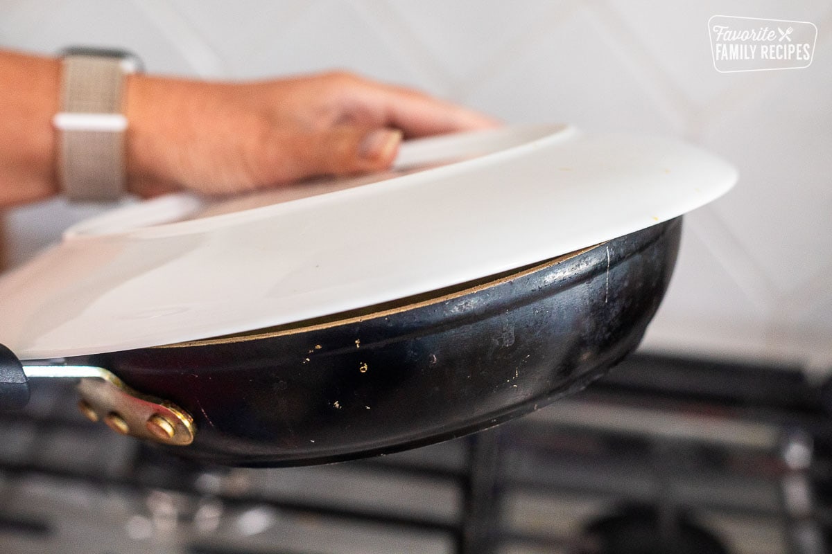 Placing a plate on top of skillet.