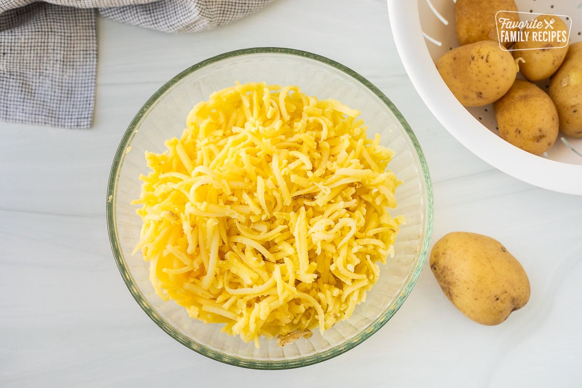 Shredded potatoes in a bowl next to colander of potatoes.