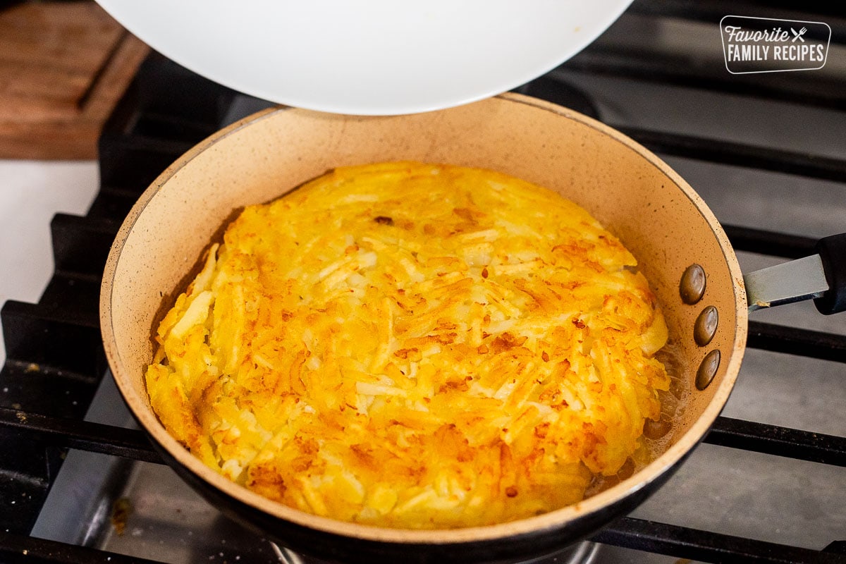 Flipped Rosti in a skillet with plate hovering above.