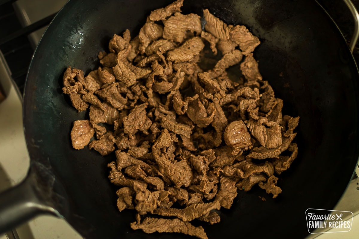 Thinly sliced beef being cooked in a wok on a stovetop