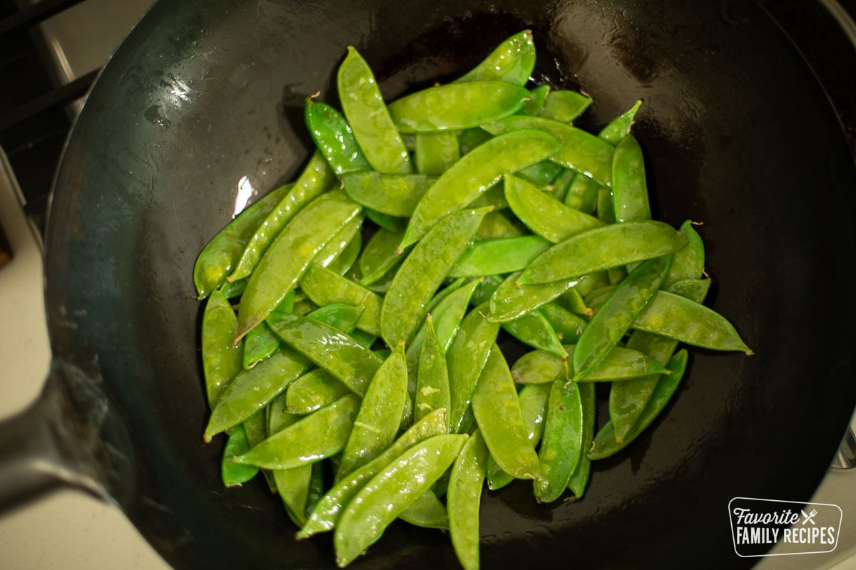 Bright green snow peas being cooked to crisp-tender in a wok on the stove