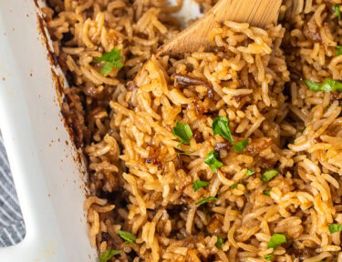 Casserole dish of Stick of Butter Rice garnished with parsley. Wooden spoon resting in the dish.