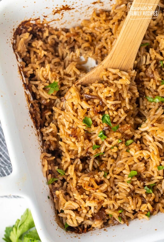 Casserole dish of Stick of Butter Rice garnished with parsley. Wooden spoon resting in the dish.