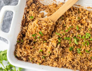 Casserole dish of Stick of Butter Rice garnished with parsley. Wooden spoon resting in the dish.