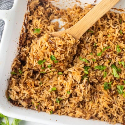 Casserole dish of Stick of Butter Rice garnished with parsley. Wooden spoon resting in the dish.