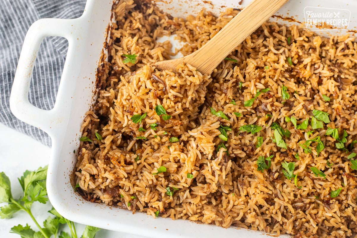 Casserole dish of Stick of Butter Rice garnished with parsley. Wooden spoon resting in the dish.