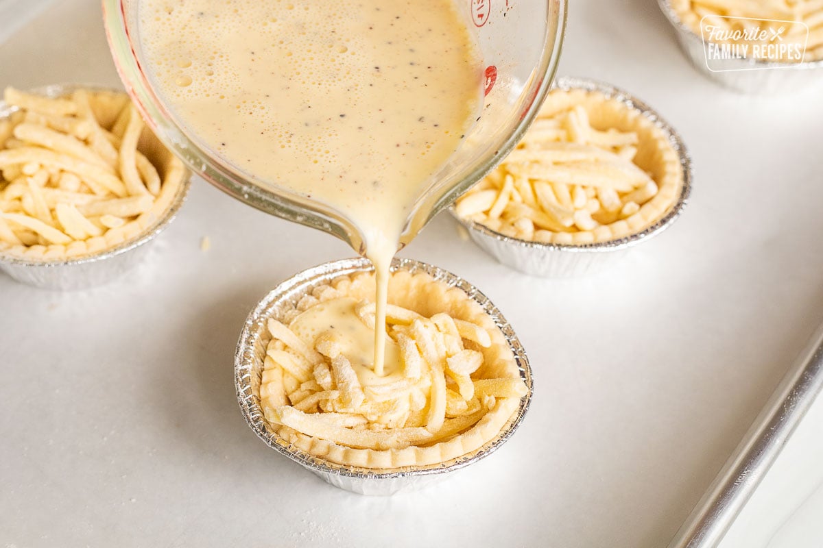 Pouring egg mixture into pie shells filled with shredded cheese.