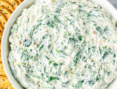 Large bowl of spinach dip next to crackers and sliced bread.