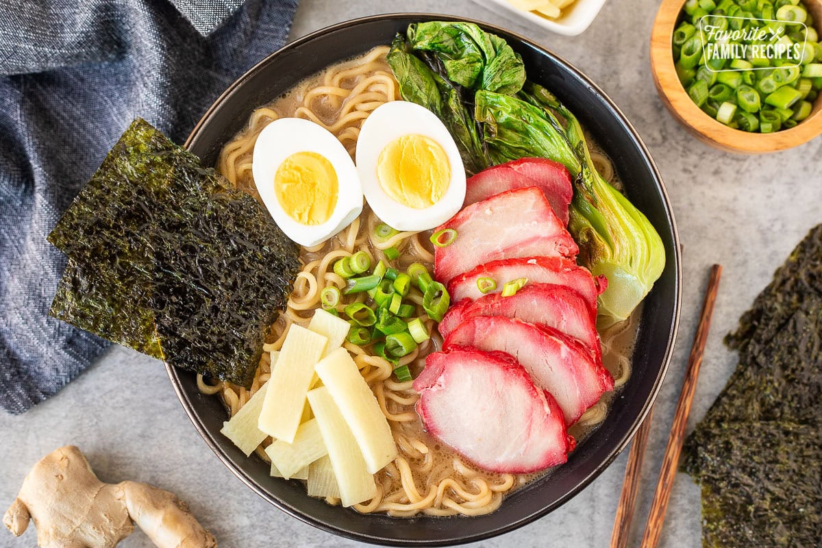 Bowl of savory Shoyu Ramen topped with barbecue pork, bok choy, sliced green onion, bamboo, boiled eggs sliced in half and seaweed sheets.