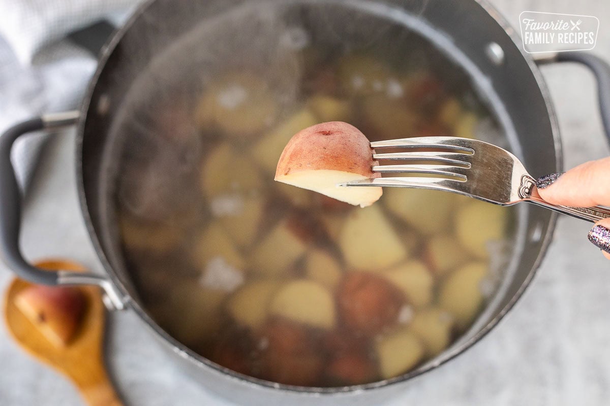 Fork poking a boiled red potato over a pot of boiling water.