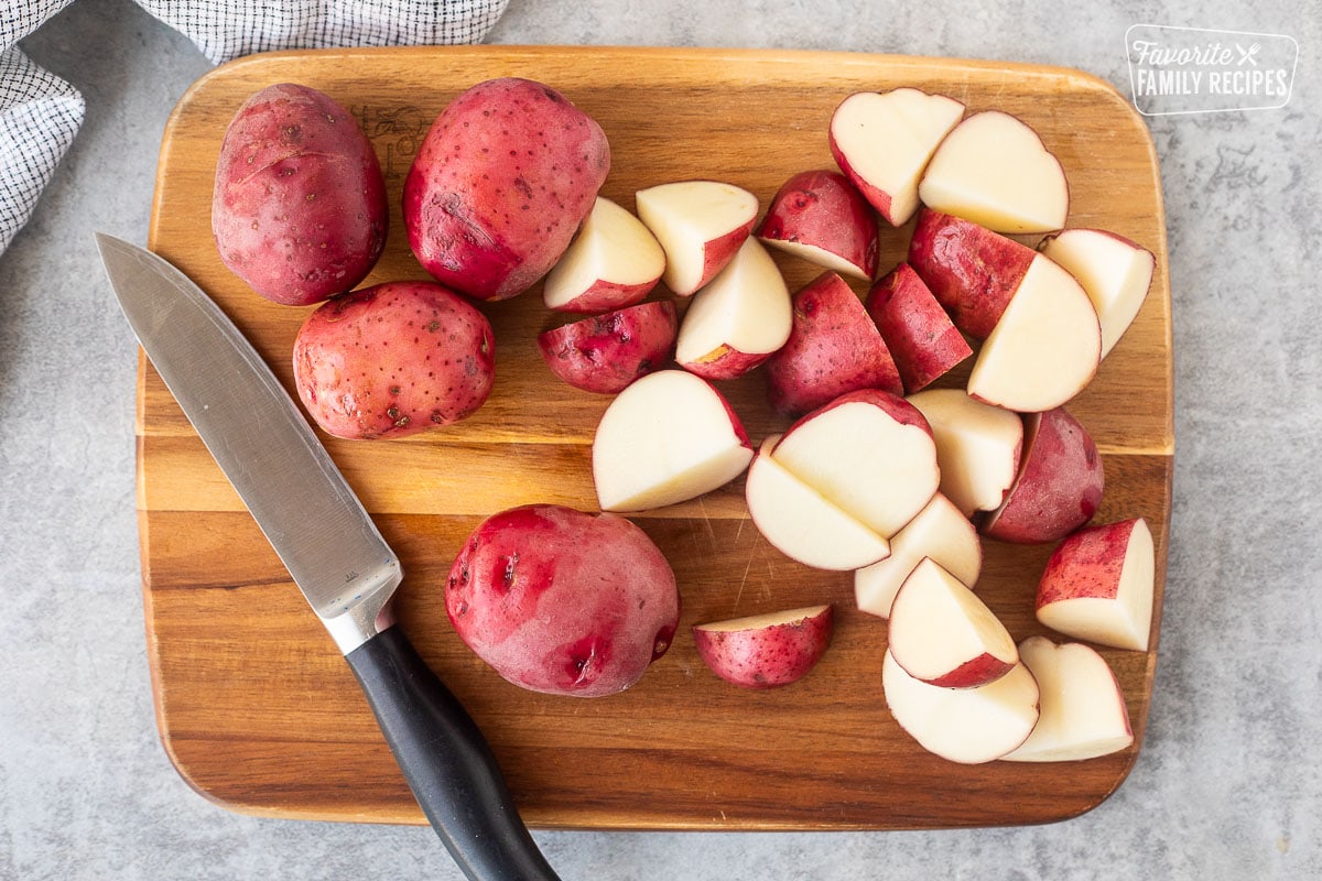 Cut red potatoes on a cutting board with a knife.