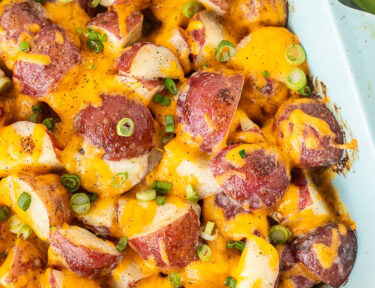 Baking dish with cheesy Ranch Potatoes topped with cheddar cheese and green onions.