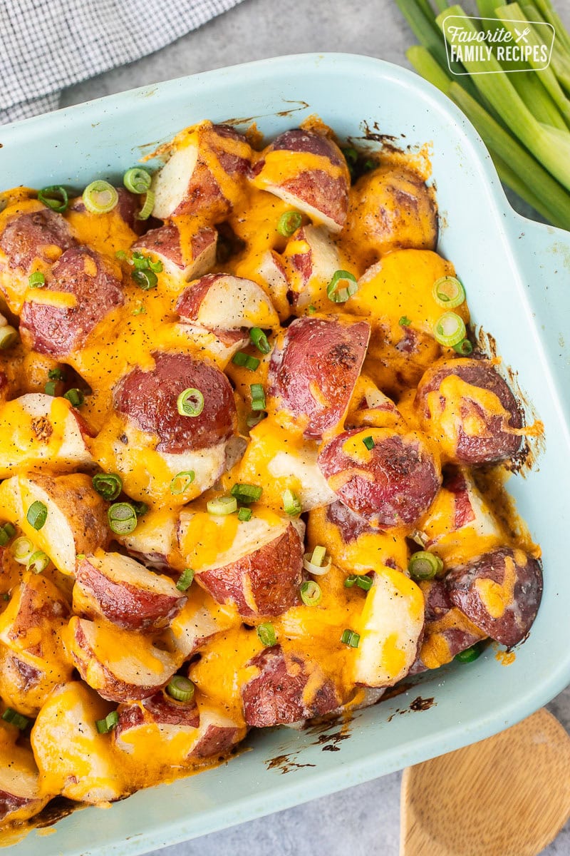 Baking dish with cheesy Ranch Potatoes topped with cheddar cheese and green onions.