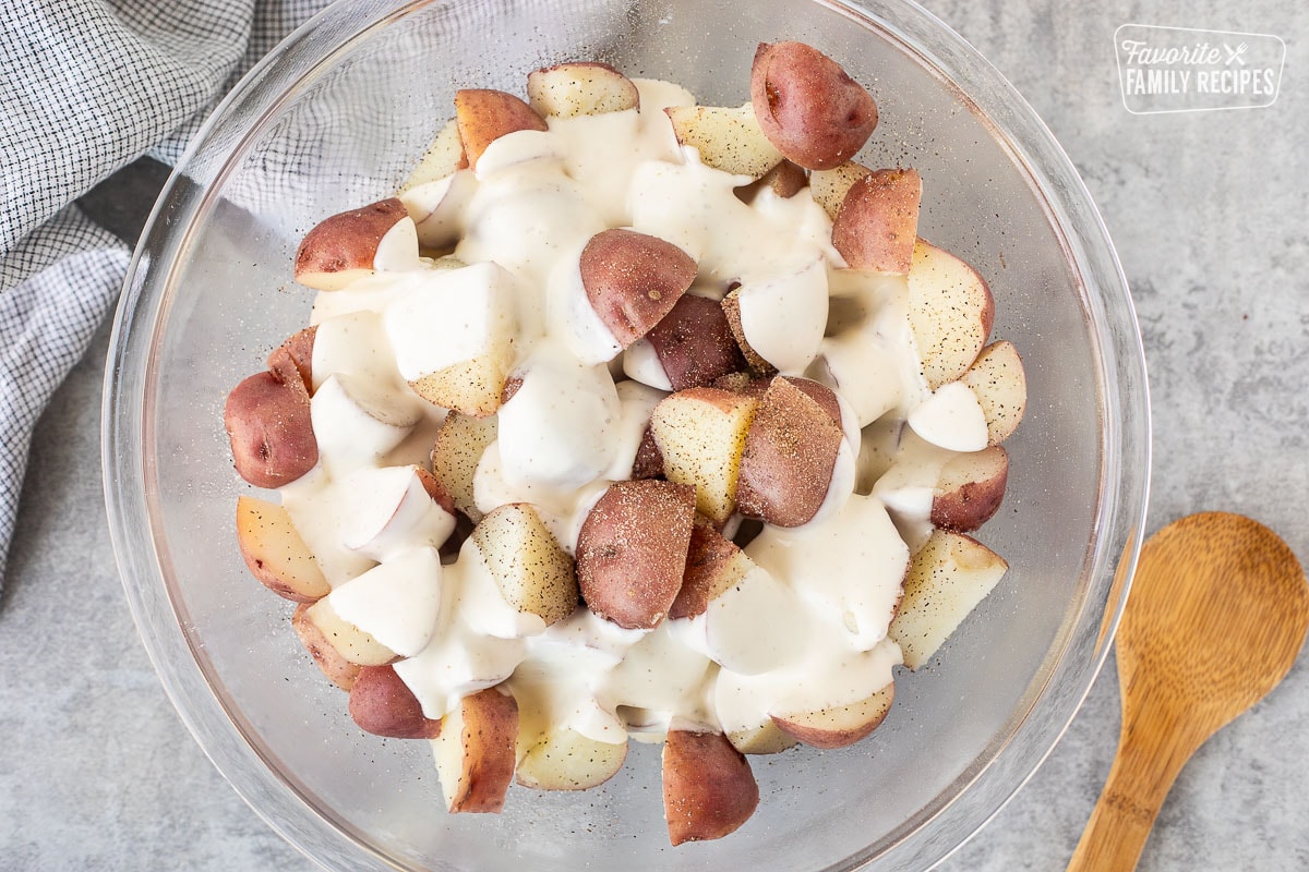 Glass mixing bowl with boiled red potatoes, ranch dressing, salt and pepper. Wooden spoon on the side.