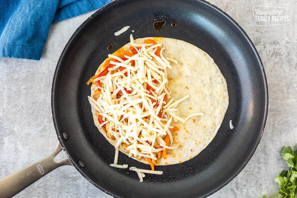 Tortilla with chicken and bell pepper filling topped with cheese in a skillet.