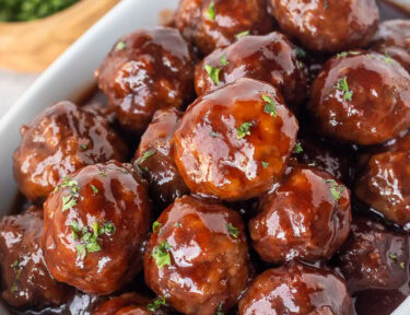 Bowl of grape jelly meatballs garnished with parsley and toothpicks on the side.