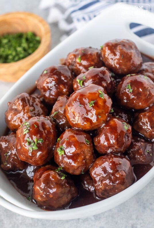 Bowl of grape jelly meatballs garnished with parsley and toothpicks on the side.