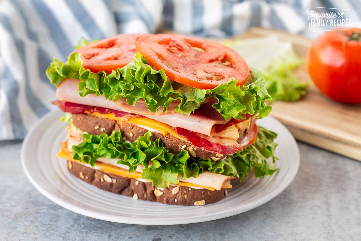 Stacked club sandwich with toasted wheat bread, mayo, cheddar cheese, turkey, bacon, ham, lettuce and tomato.