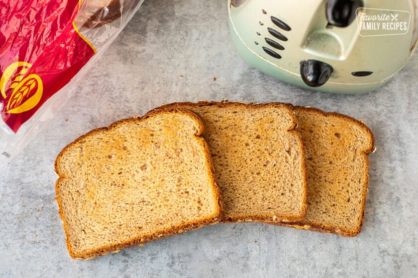 Three slices of toasted wheat bread next to a toaster.