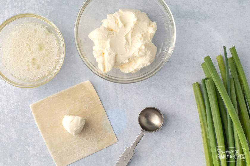 Cream cheese filling on a wonton wrapper next to a bowl of cream cheese and a bowl of beaten egg whites.