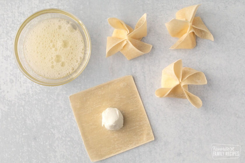 Uncooked cream cheese wontons with one laying flat with cream cheese in the middle.