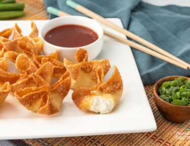 Close up of golden fried cream cheese wontons with one showing the creamy center