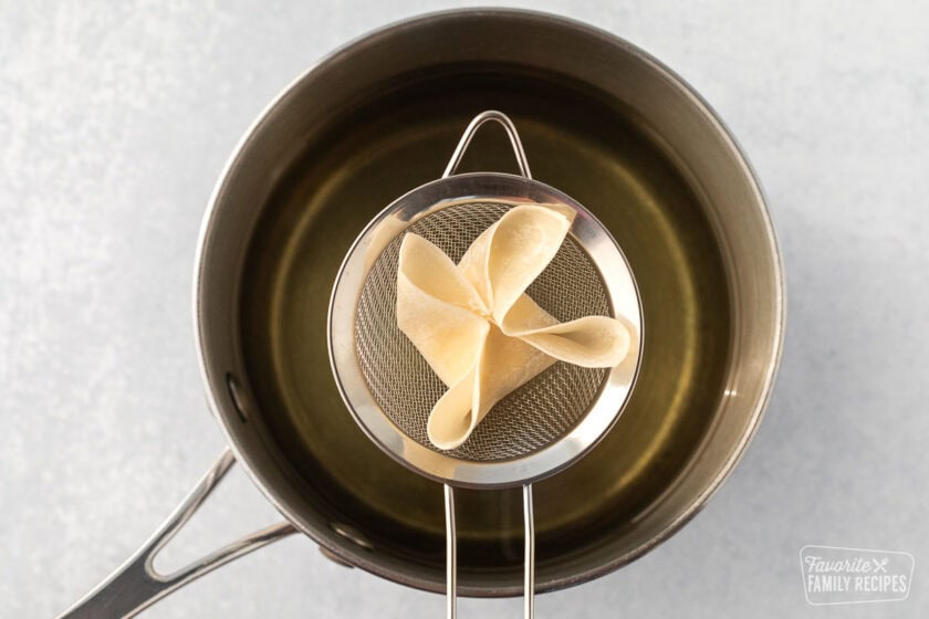 Cream cheese wonton being lowered into hot oil.