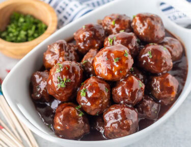 Grape jelly meatballs garnished with fresh parsley on top. Toothpicks on the side.