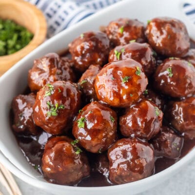 Grape jelly meatballs garnished with fresh parsley on top. Toothpicks on the side.