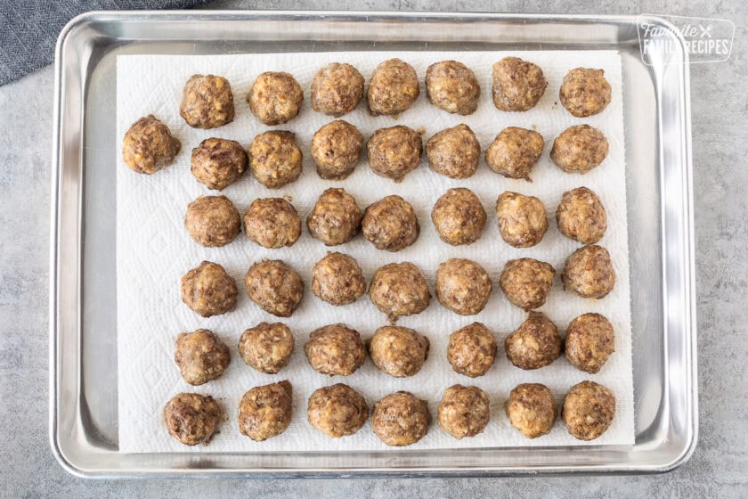 Meatballs that have been baked on a lined cookie sheet being prepared to be frozen