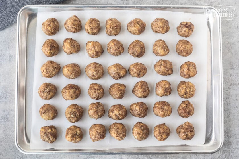 Meatballs that have been baked on a lined cookie sheet that have been frozen and ready to be bagged