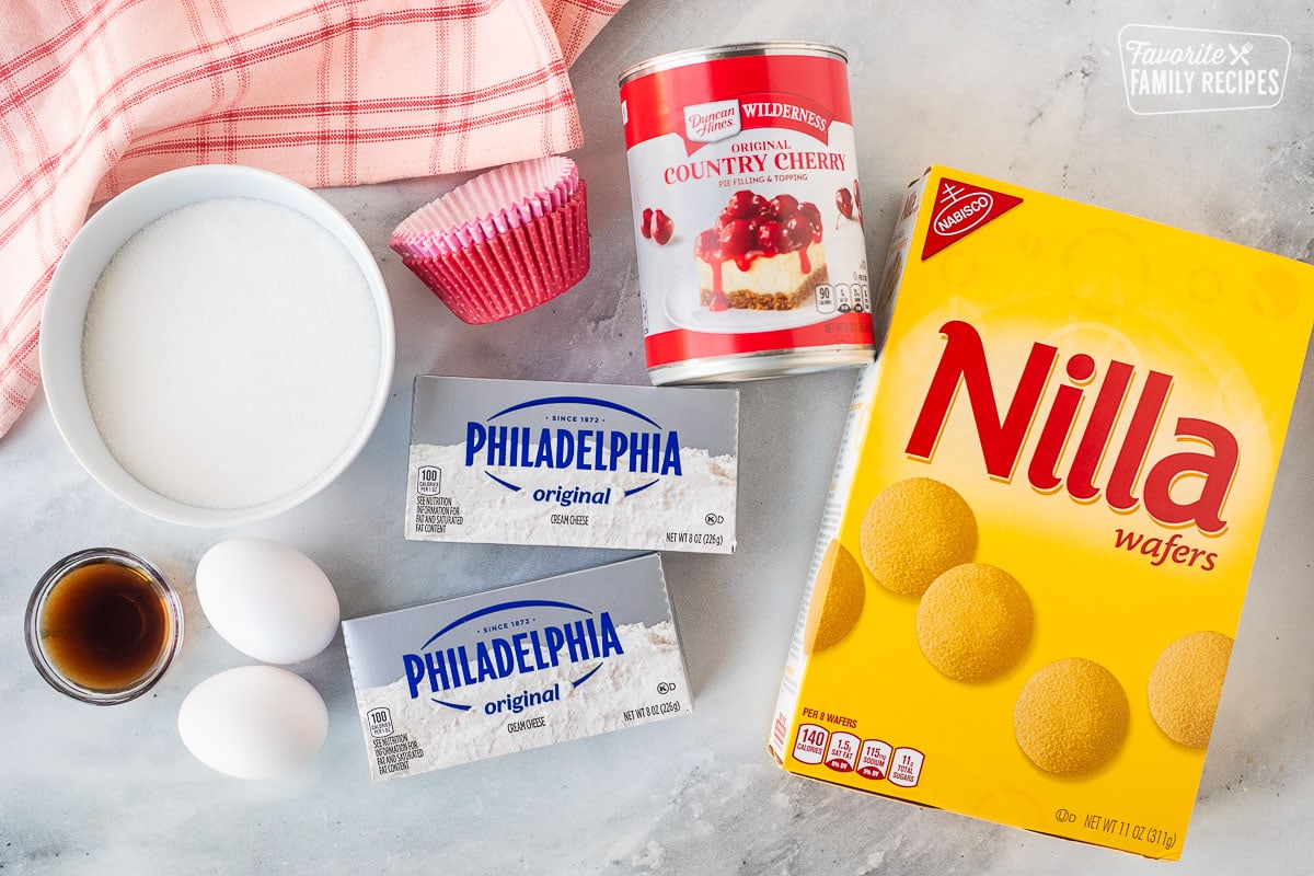 Ingredients for mini cherry cheesecakes like Nilla wafers, cream cheese, and canned cherry filling.