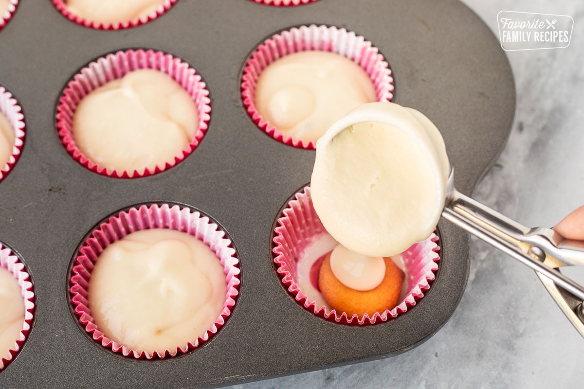 A spoon adding cheesecake batter to mini baking cups.