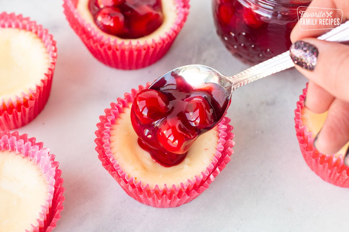 Someone spooning cherries on top of a mini cheesecake.