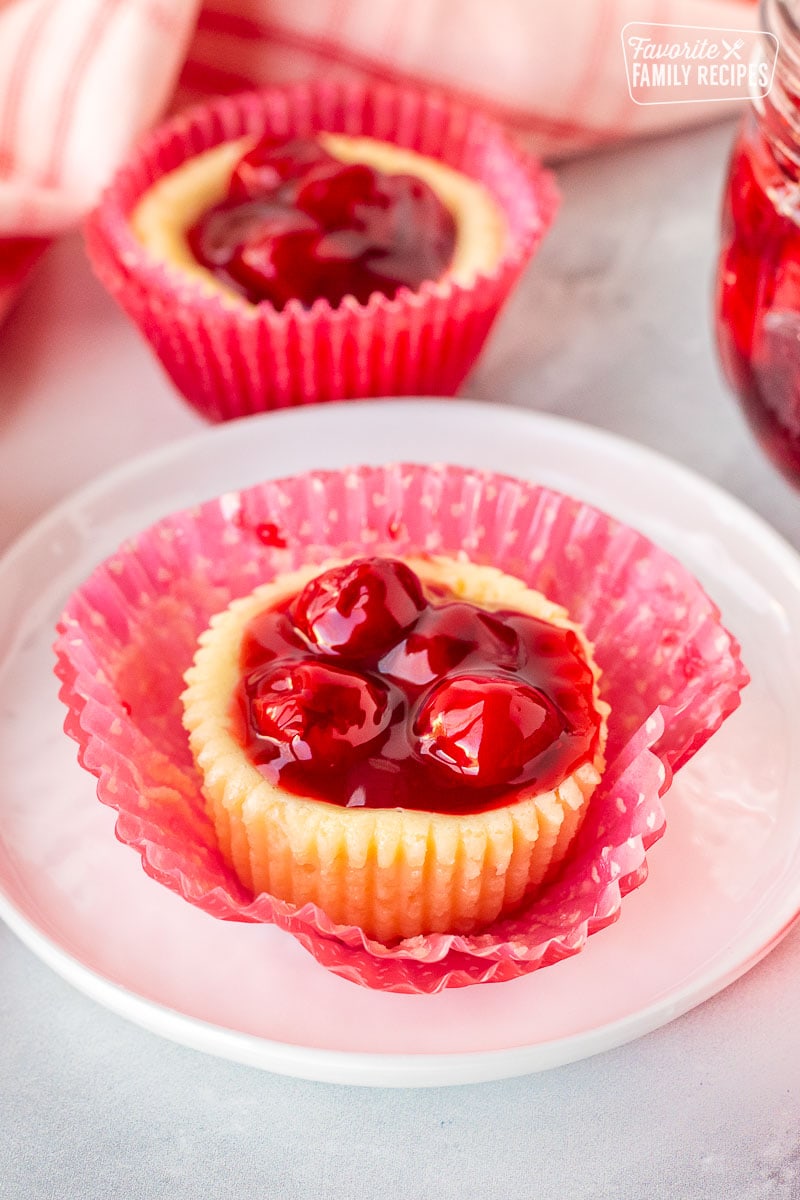 A close up of an unwrapped mini cherry cheesecake on a small plate.