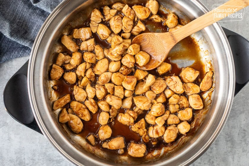 Skillet with cooked teriyaki chicken and wooden spoon.