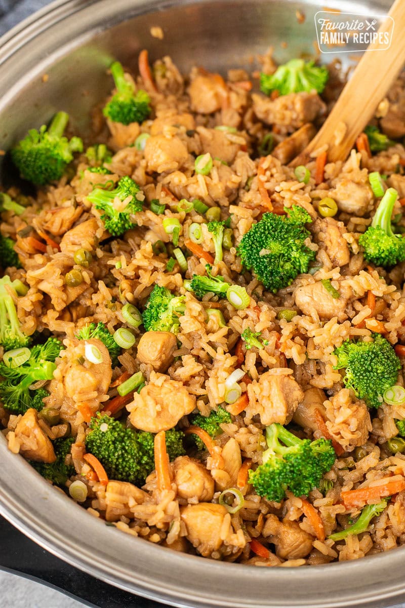 Skillet of one Pot Teriyaki Chicken Bowls with fried rice, chicken, broccoli , carrots, and green onion, stirred with a wooden spoon.