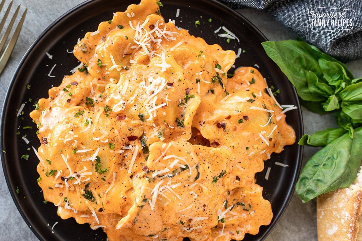 Plate with fresh ravioli tossed in a ravioli sauce and fresh shredded cheese on top.