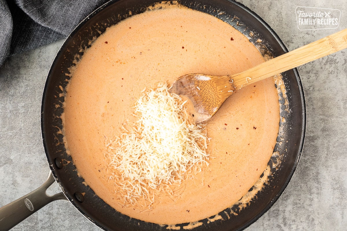 Skillet with ravioli sauce space and shredded cheese and wooden spoon.