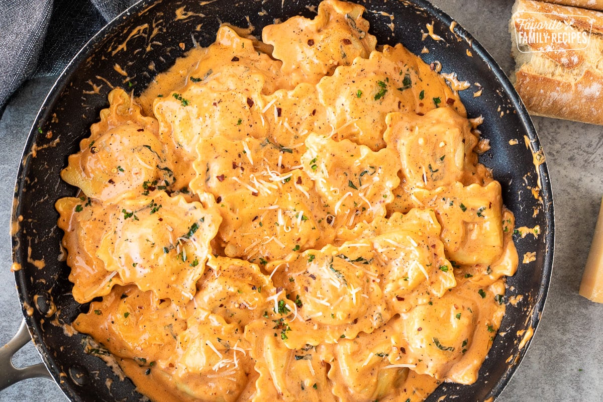 Ravioli tossed in ravioli sauce in a skillet.