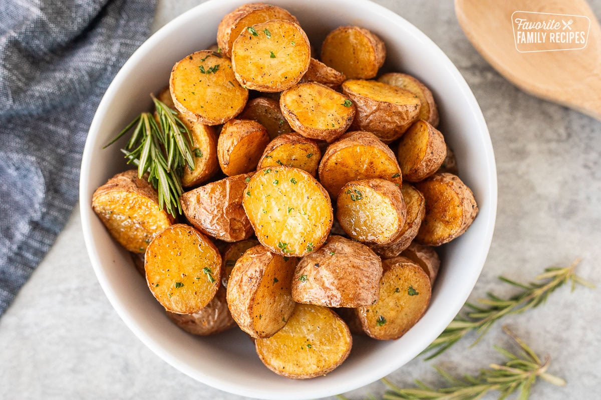 Roasted red potatoes in a bowl garnished with parsley and rosemary.