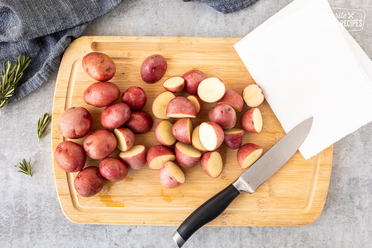 Cutting board with cut red potatoes, knife and paper towel.