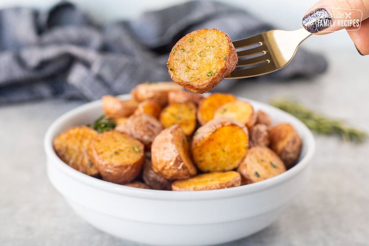 Fork with Roasted red potato over a bowl. Garnished with parsley and rosemary.